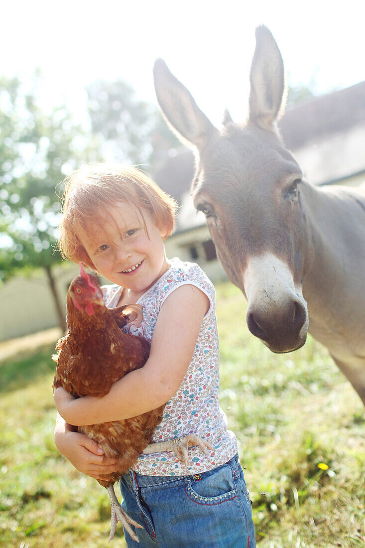Young ginger girl carrying a chicken next to a donkey in the country
