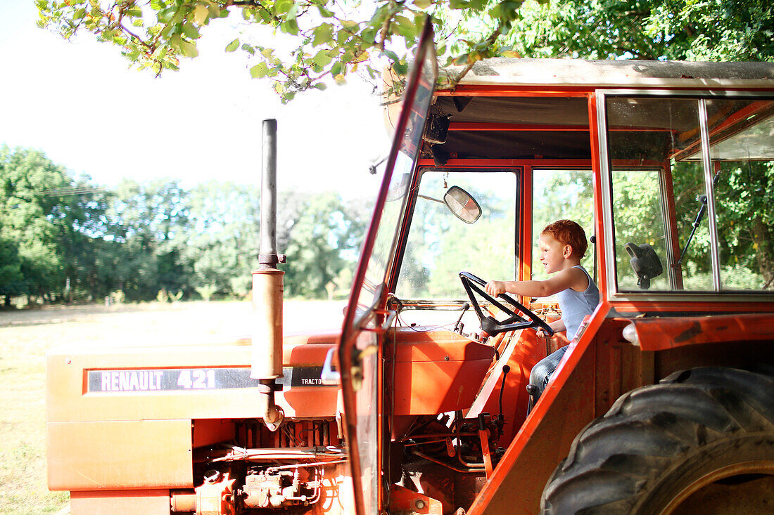 Young boy driving a tractor in summer in the country