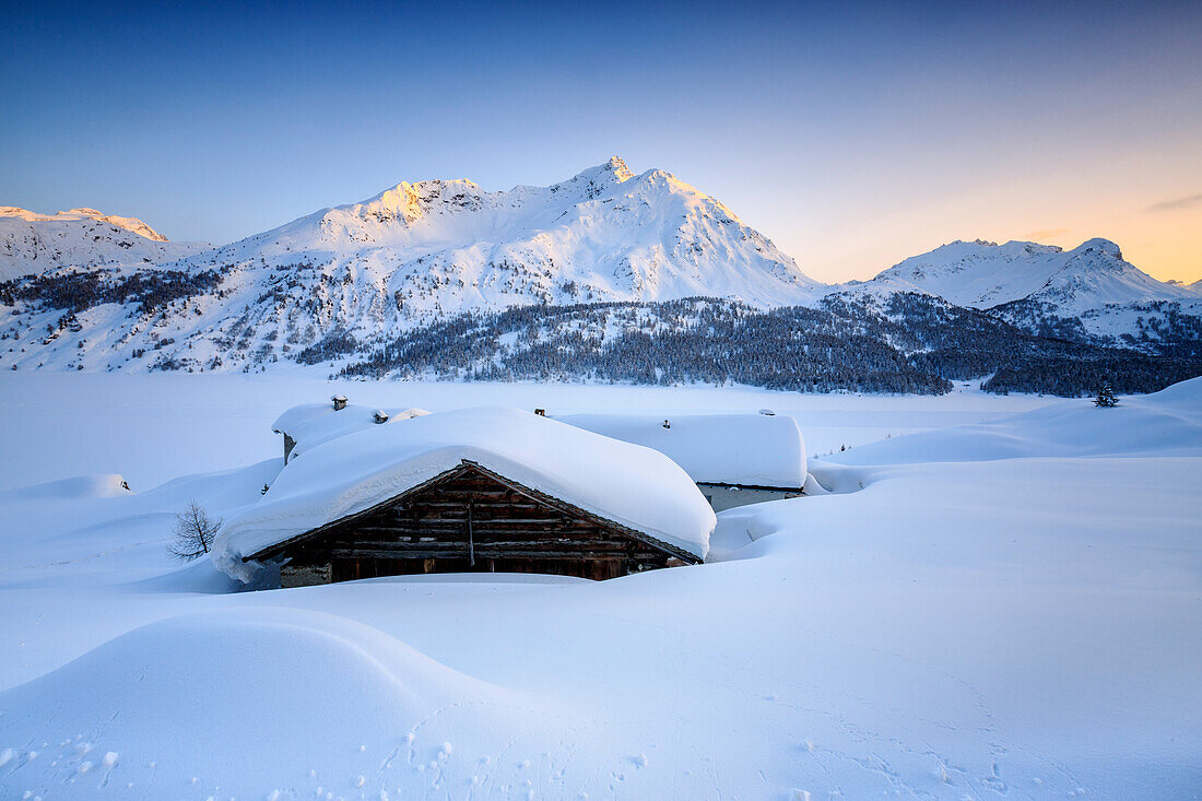 Some scattered huts in a snowy landscape at Spluga by the Maloja Pass with the magical colors of the sunset, Graubunden, Swiss Alps, Switzerland, Europe