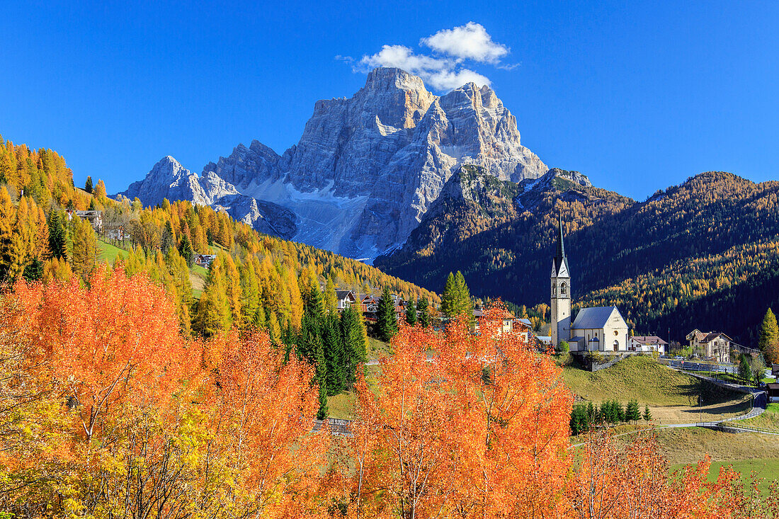 Red and orange trees with the tiny church of Selva di Cadore, in the Dolomites, with Mount Pelmo in the background, Veneto, Italy, Europe