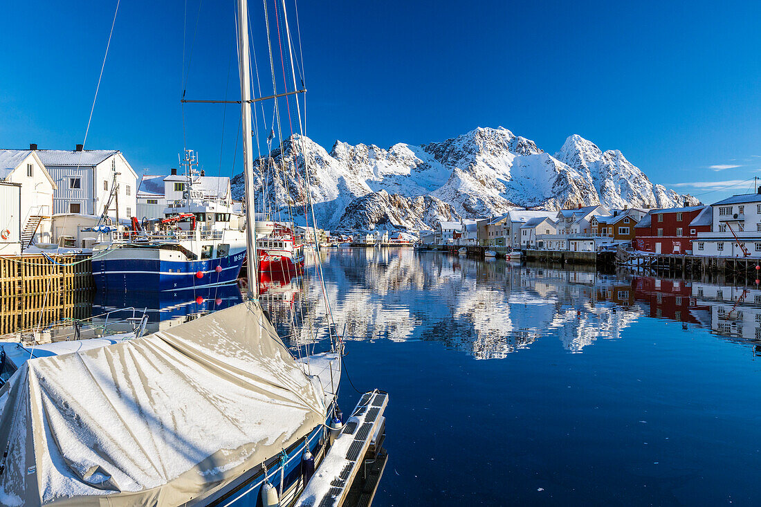 Boats docked in the calm waters of the port of Henningsvaer with the reflection of fishermen's houses and Norwegian Alps, Lofoten Islands, Arctic, Norway, Scandinavia, Europe