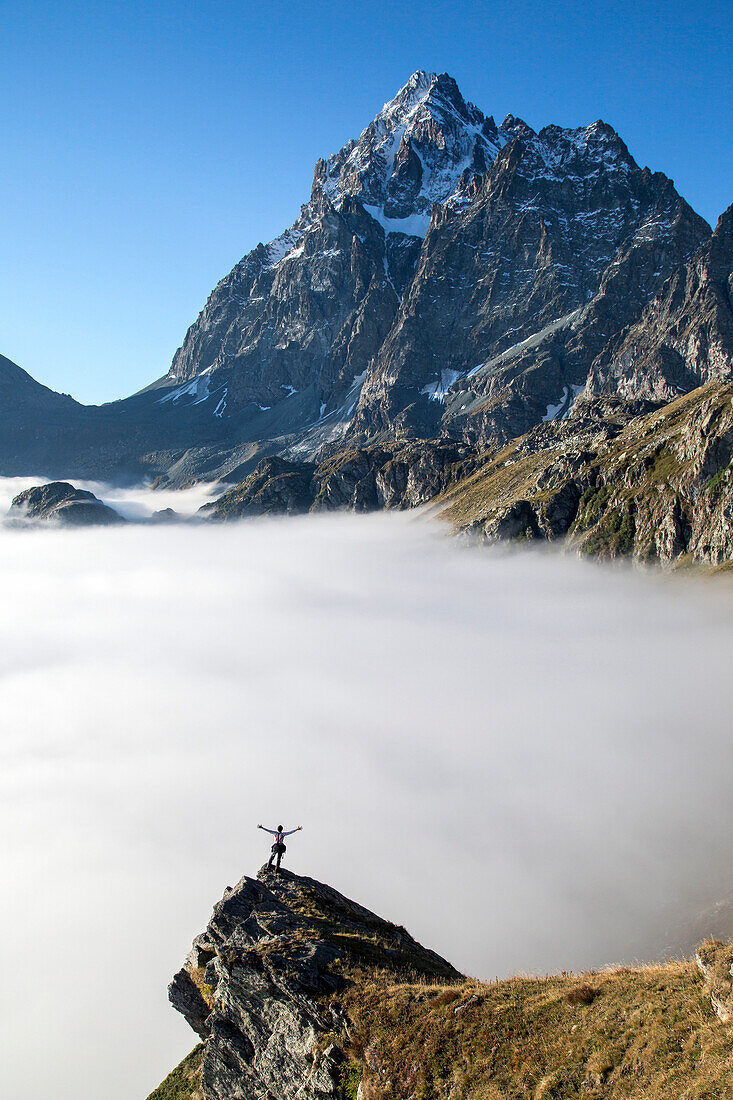 A hiker contemplating the Monviso Massif rising above a bed of clouds in the Cottian Alps, Piedmont, Italy, Europe