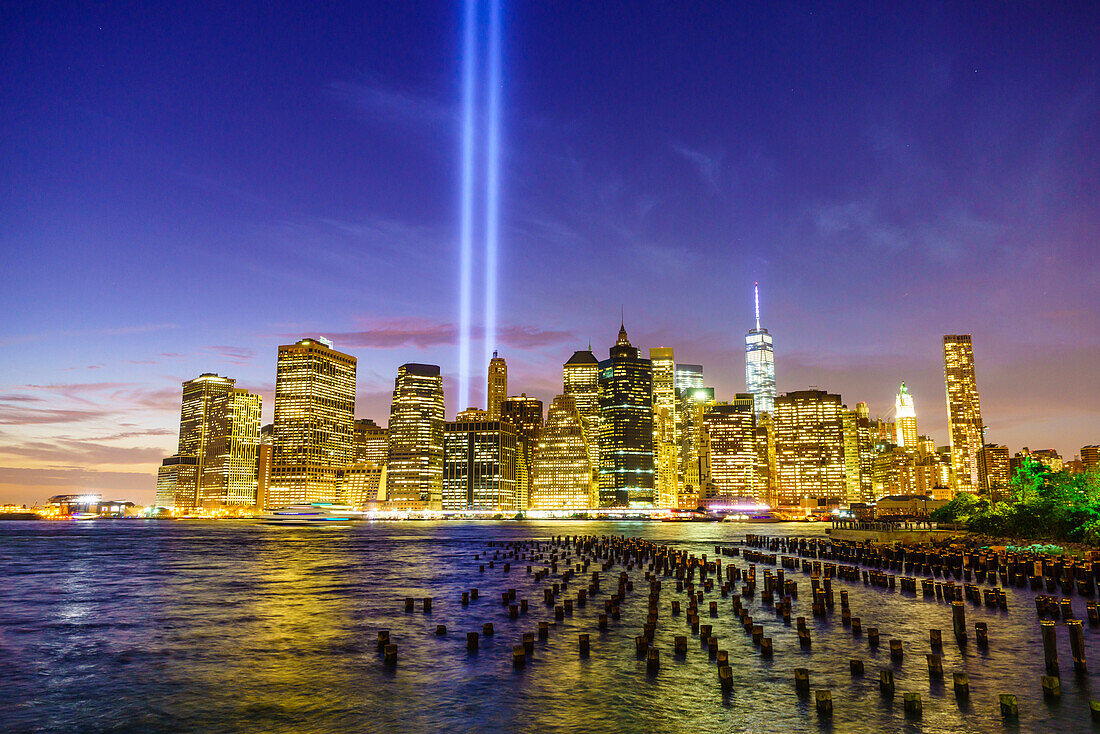 Lower Manhattan skyscrapers including One World Trade Center from across the East River at night, with light beams from the Tribute in Light 9/11 Memorial, New York City, New York, United States of America, North America