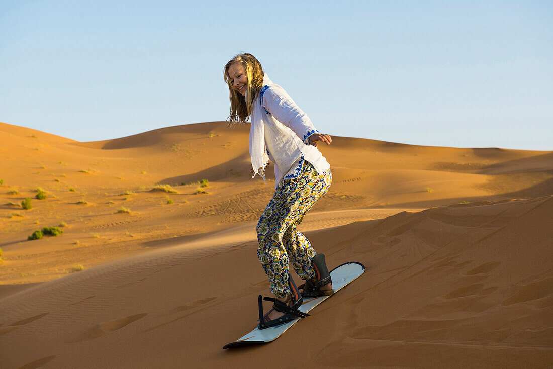 young woman with snowboard, sand dunes near Merzouga, Erg Chebbi, Sahara Desert, Morocco, Africa