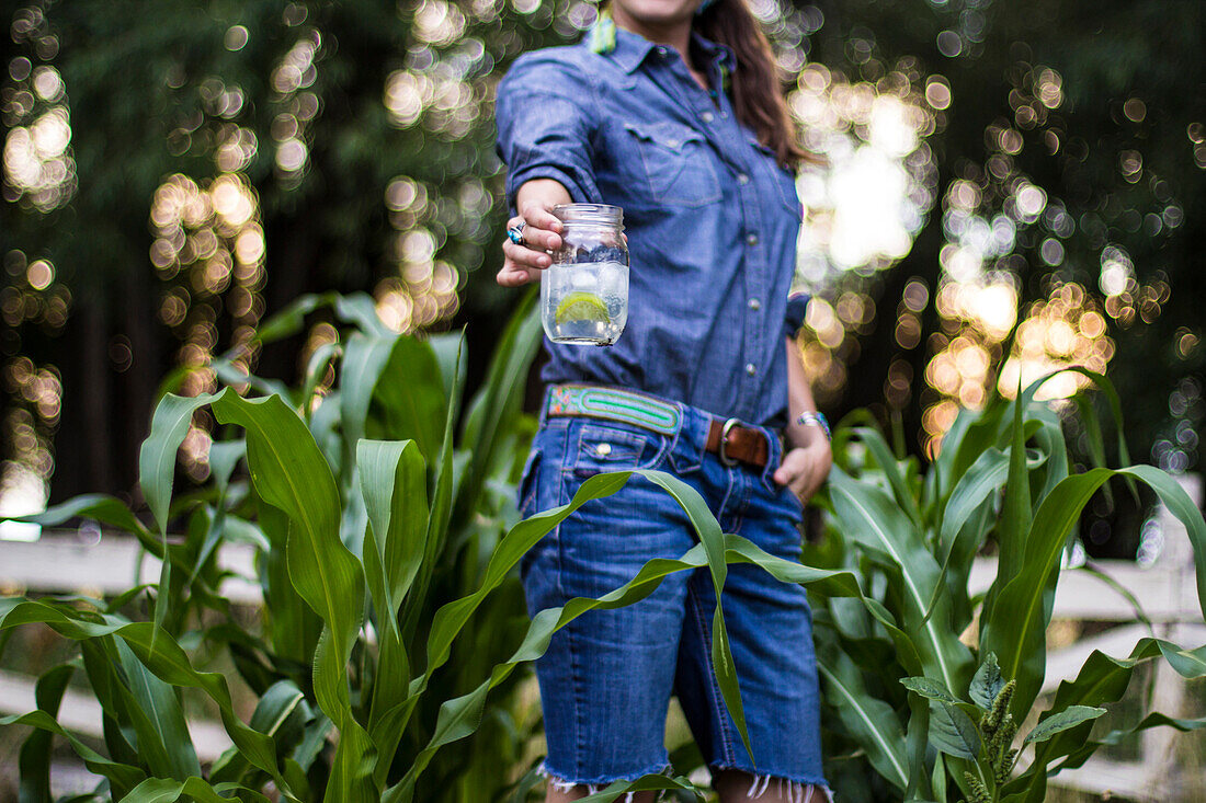 Woman stands in her garden drinking a gin and tonic during the summer.