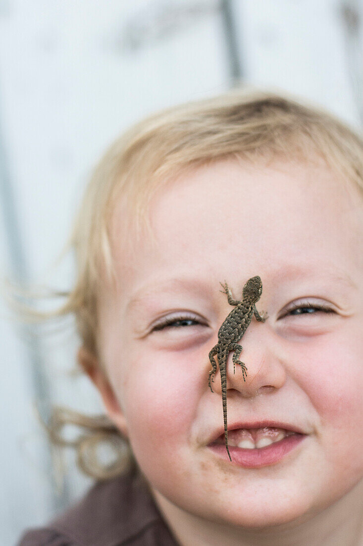 Toddler girl smiles at camera with Sagebrush lizard on nose in Chico, California.