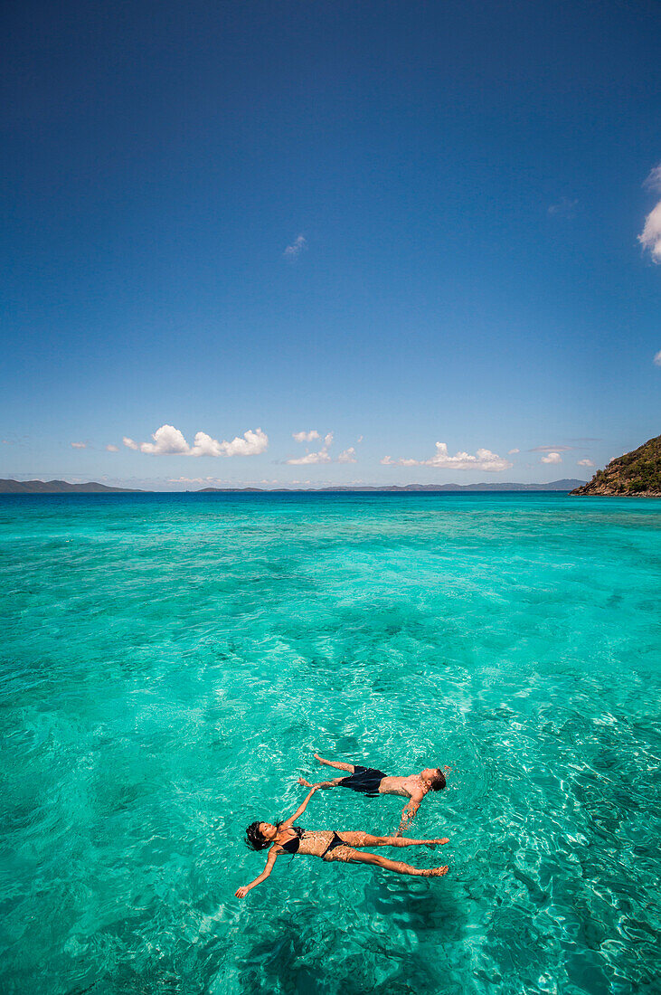 A couple float on their backs in clear teal Caribbean water.