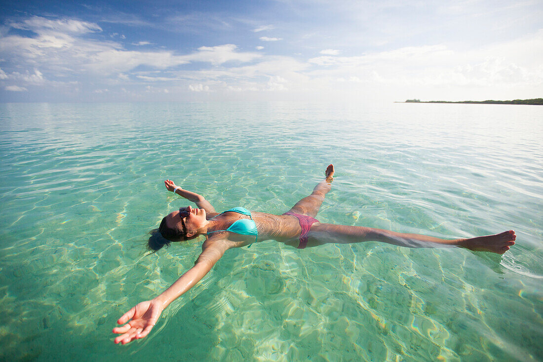 A young woman floats on her back with her limbs stretched out in shallow turquoise water while on vacation in Cayo Coco, Cuba.