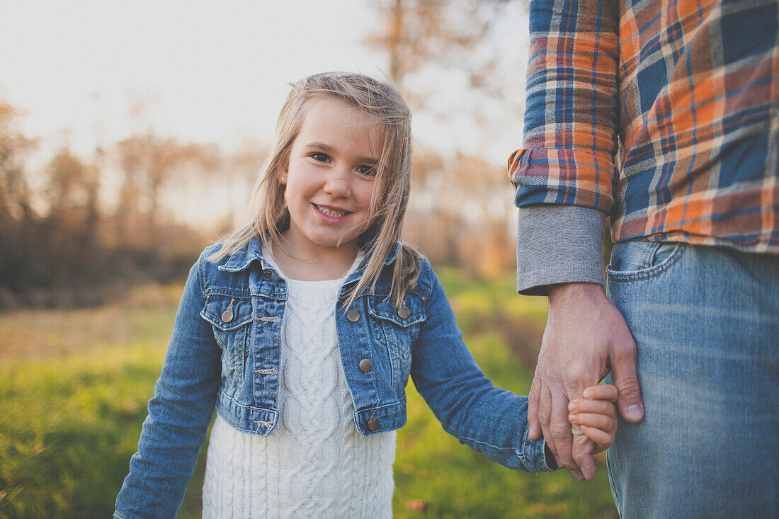 A father holds hands with his young daughter.