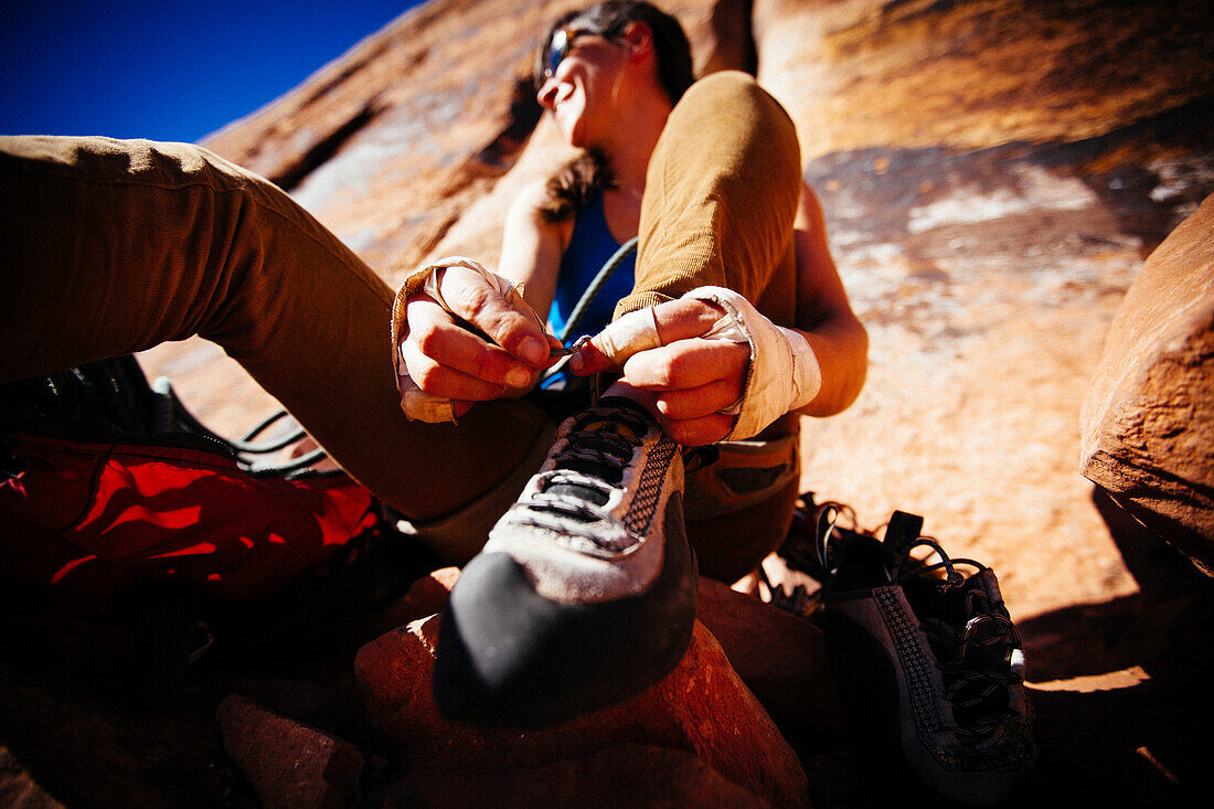 A woman ties her rock climing shoes as she gets ready for her next climb. Indian Creek, Utah