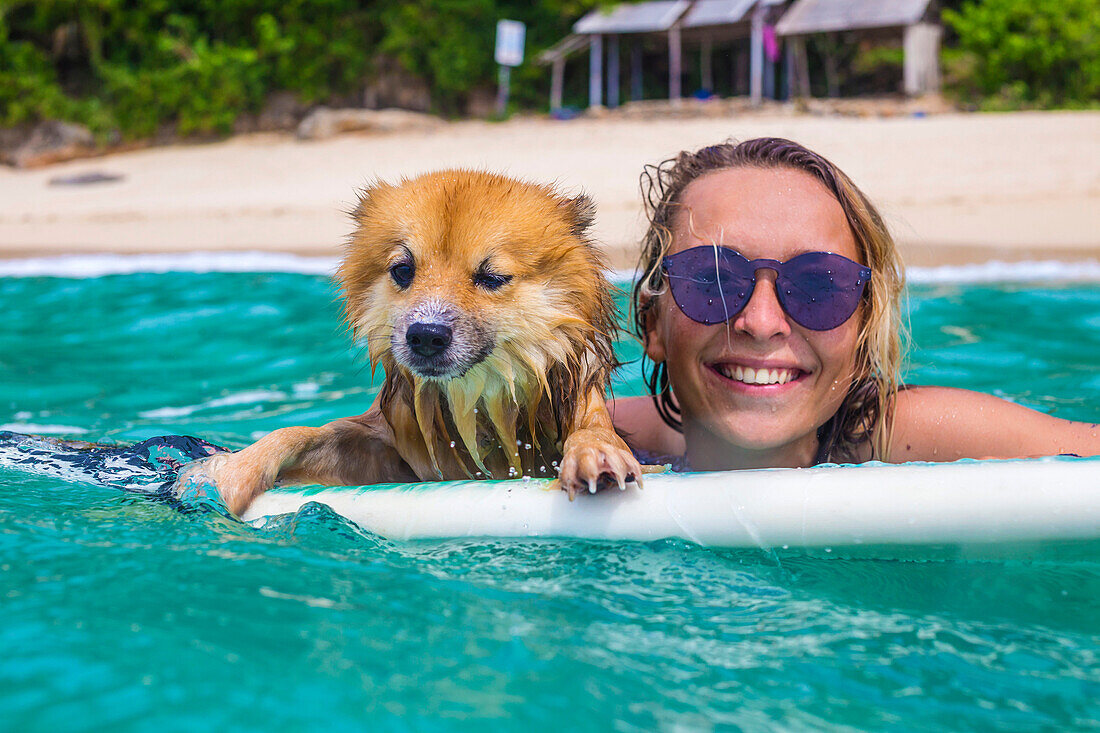 Surfer girl and funny dog in ocean water.