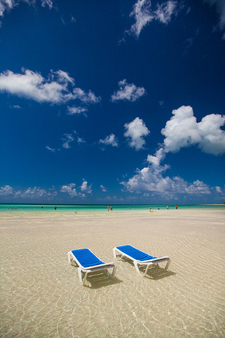 Two empty beach chairs sit in ankle deep water facing the turquoise ocean in Cayo Coco, Cuba.