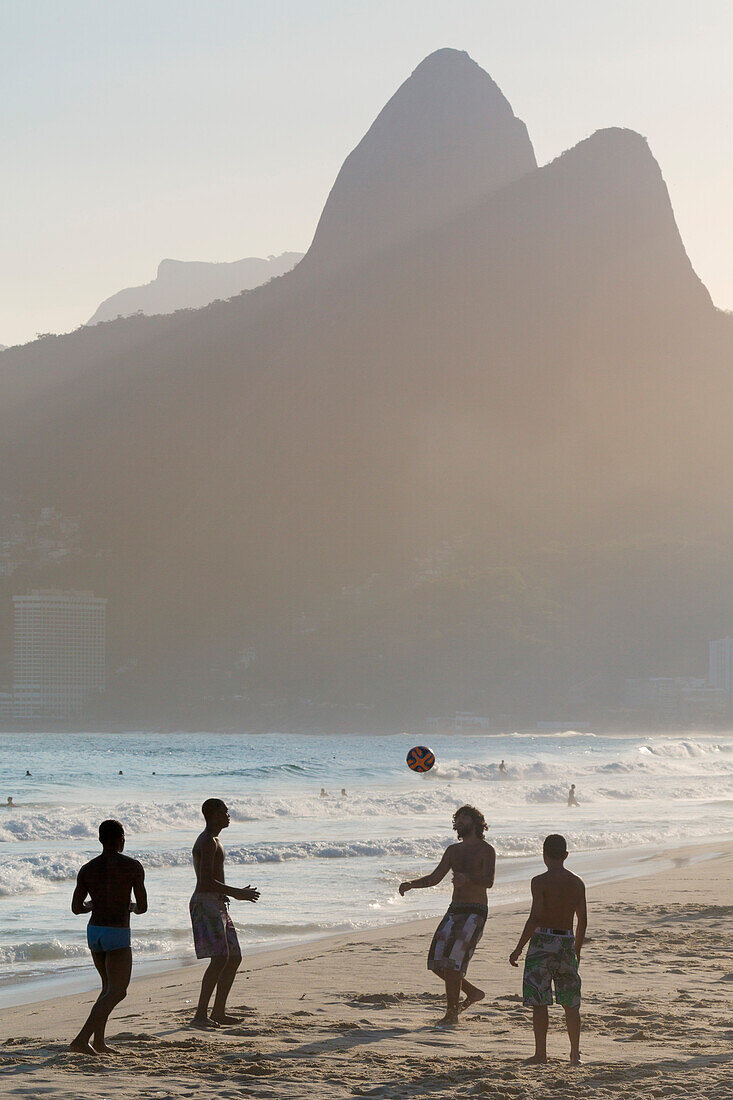 Locals playing football on Ipanema beach with the Morro dos Dois Irmaos (Two Brothers) mountains behind, Rio de Janeiro, Brazil, South America