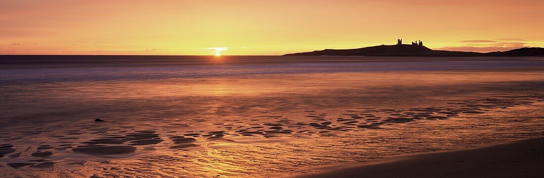 Dunstanburgh castle at sunrise, view across Embleton Bay, Northumberland, England, United Kingdom, Europe