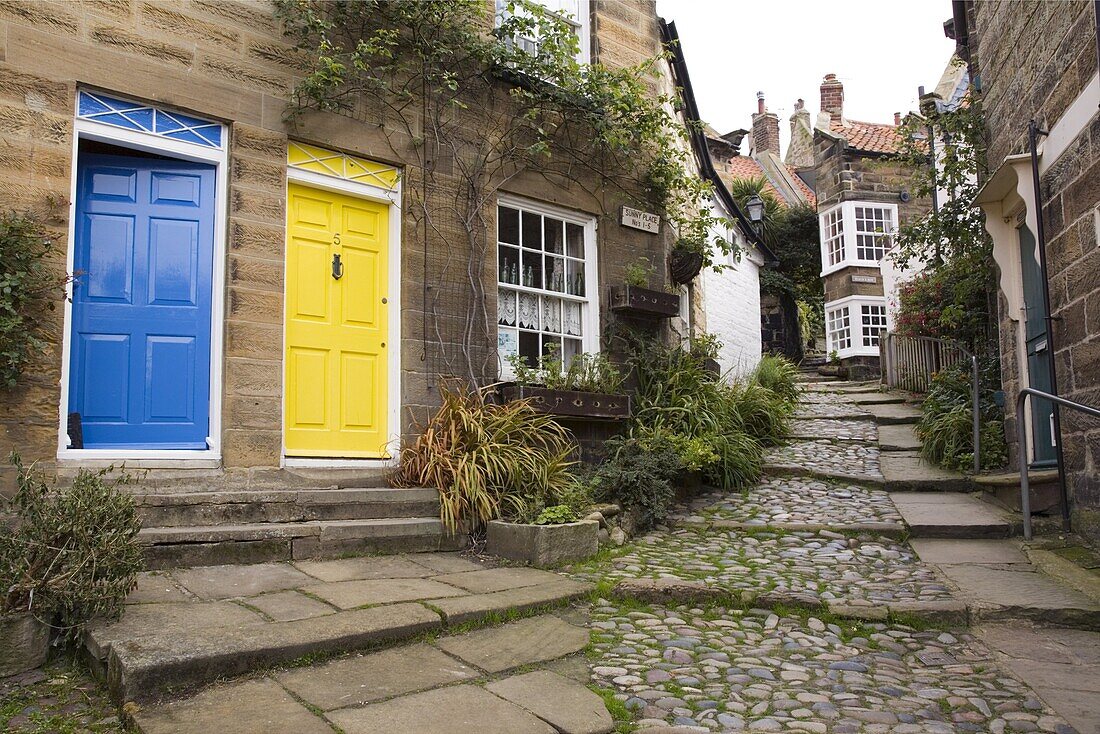 Yellow and blue doors on houses in The Opening, a narrow stepped cobbled alley on steep hill in Old Bay part of the fishing village, Robin Hood's Bay, Yorkshire, England, United Kingdom, Europe