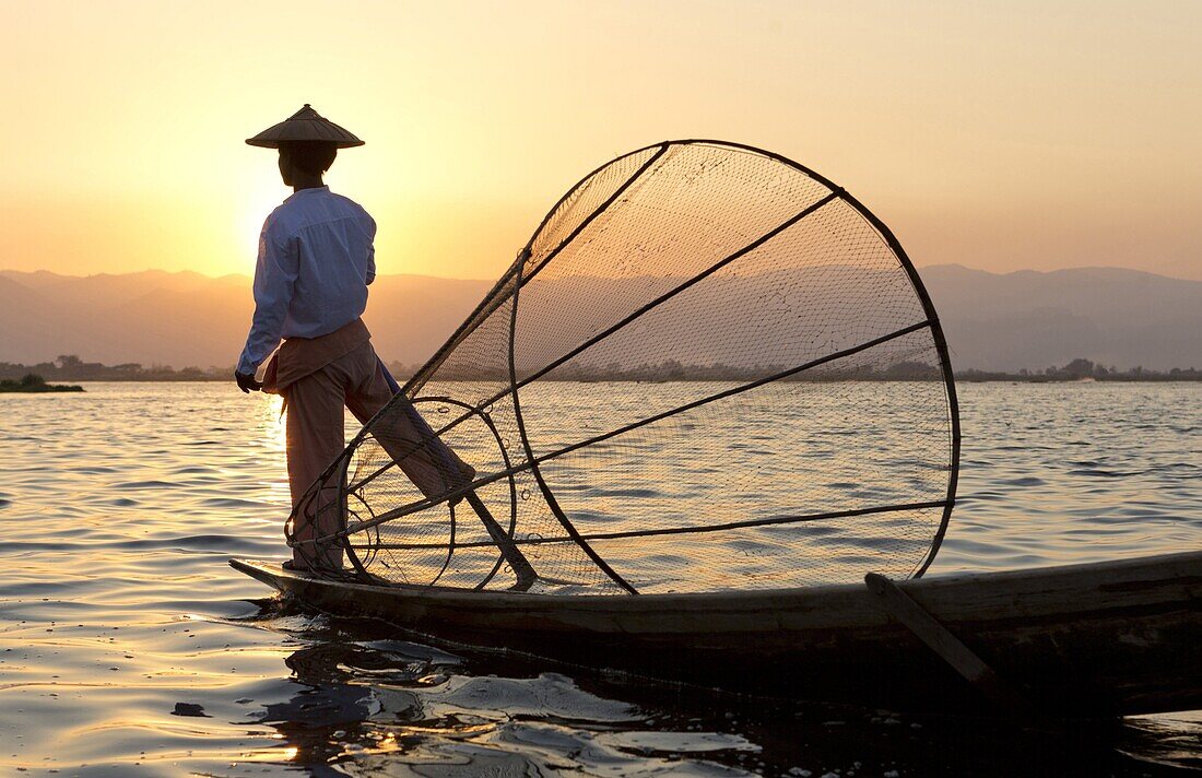 Intha 'leg rowing' fishermen at sunset on Inle Lake who row traditional wooden boats using their leg and fish using nets stretched over conical bamboo frames, Inle Lake, Myanmar (Burma), Southeast Asia