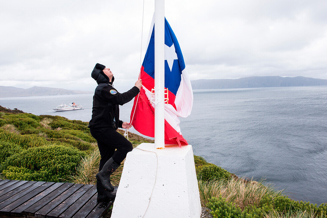 Ein Offizier der Armada de Chile Marine hisst die chilenische Flagge an der chilenischen Wetterstation, Kap Hoorn, Kap Hoorn Nationalpark, Magallanes y de la Antartica Chilena, Patagonien, Chile, Südamerika