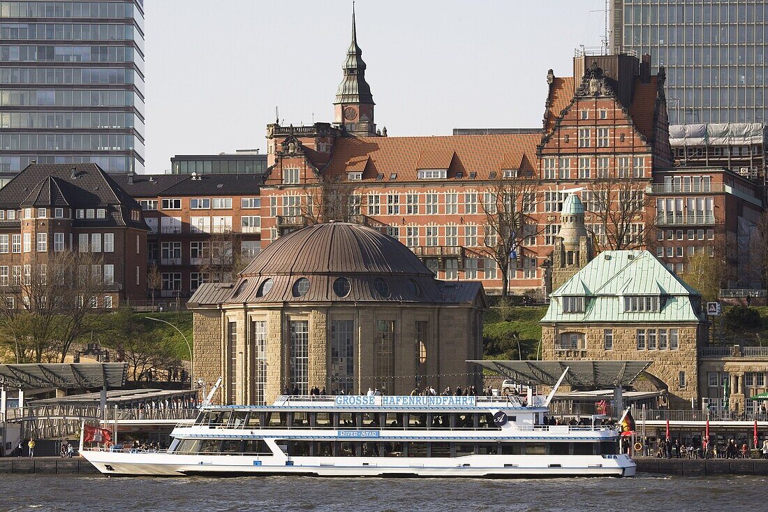 A tour boat docks by the St. Pauli Landing Stages (Landungsbruecken) while buildings of St. Pauli overlook the harbour in Hamburg, Germany, Europe