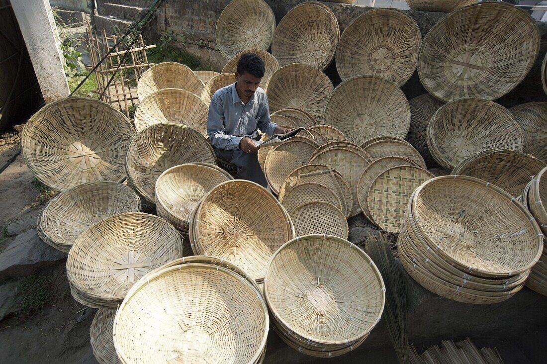 Basketmaker reading newspaper whilst waiting for customers in early morning market on the banks of the Brahmaputra river, Guwahati, Assam, India, Asia