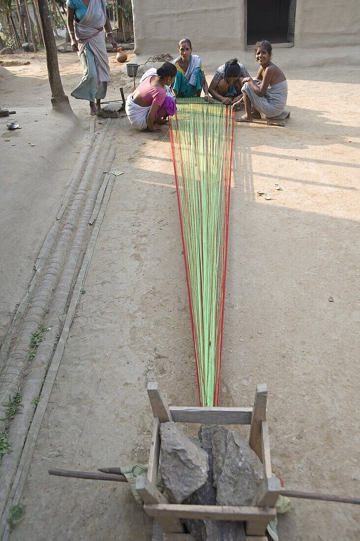 Village women in communal area preparing sari length of coloured cotton for weaving, Ganeshpahar village, Assam, India, Asia