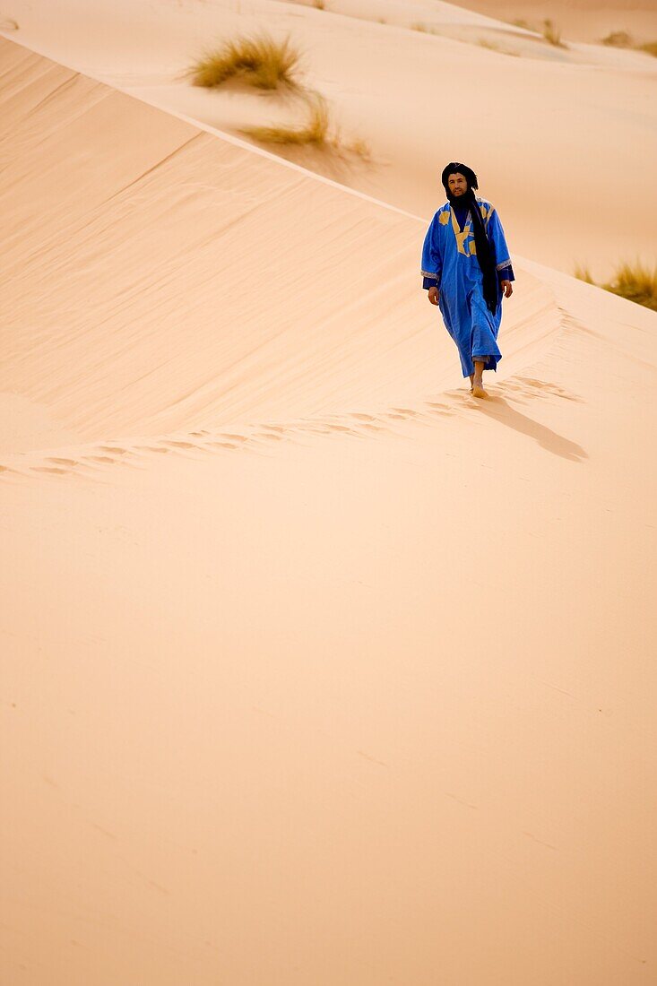 Berber man in blue robe walking along the ridge of a sand dune in the Erg Chebbi sand sea near Merzouga, Morocco, North Africa, Africa
