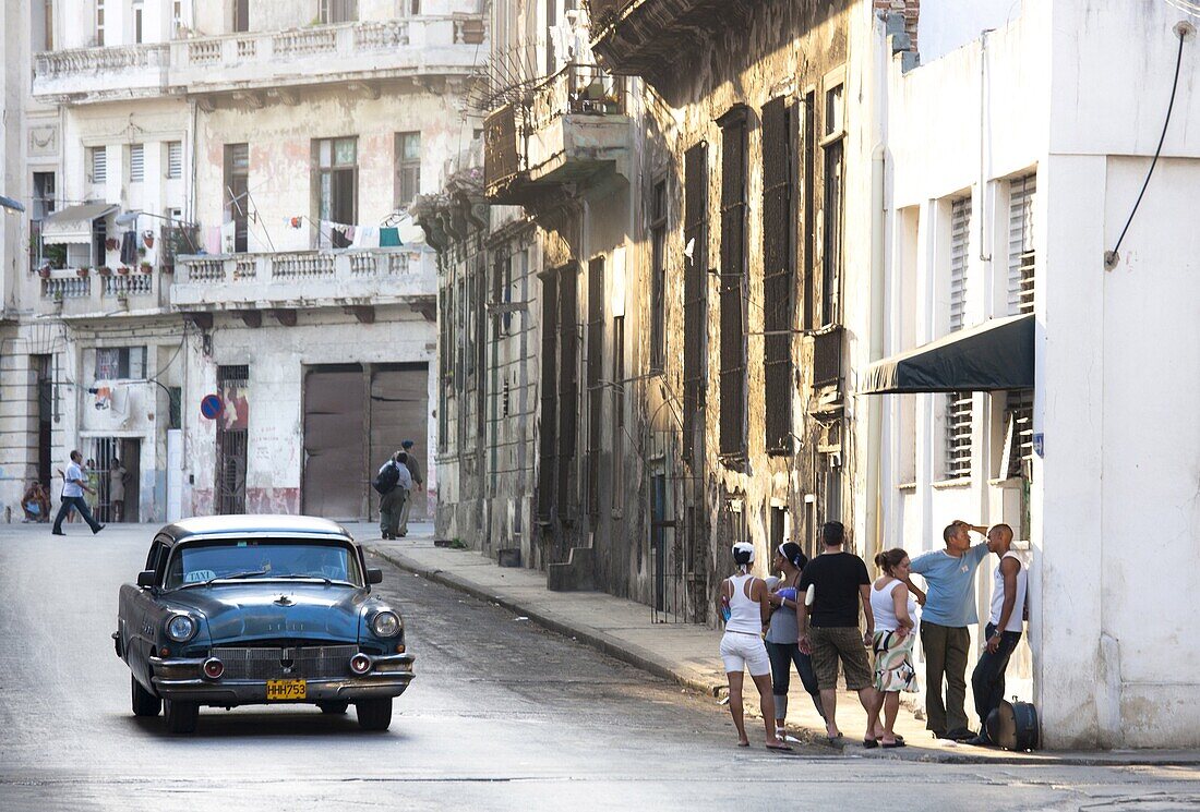 Street scene showing old American car operating as taxi for local people and a queue of people outside a shop, Havana, Cuba, West Indies, Central America