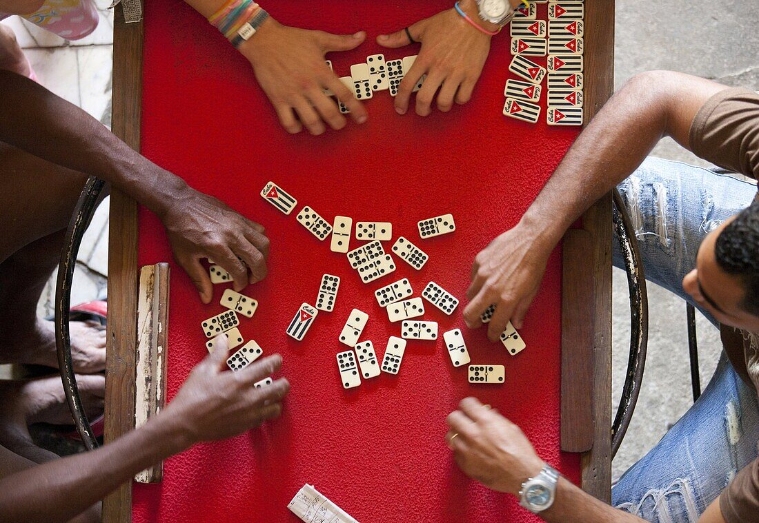 Overhead view of four people playing dominos on a red table using dominos marked with Cuba and the Cuban flag, Havana, Cuba, West Indies, Central America