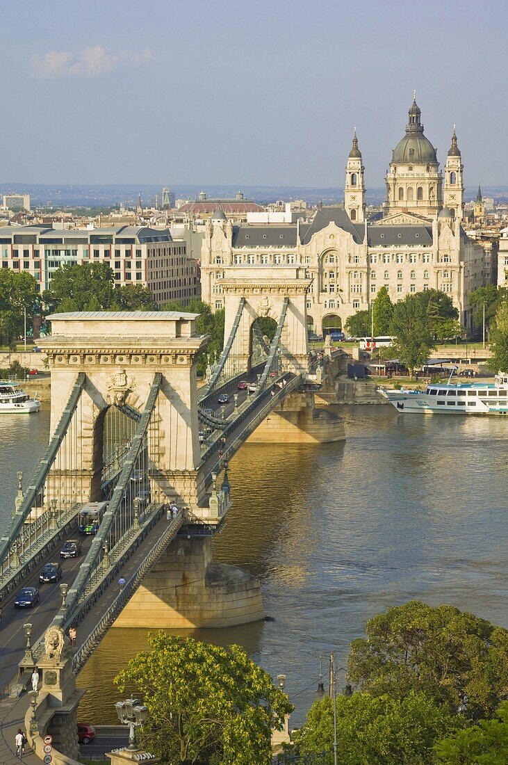Traffic driving over the River Danube, on The Chain Bridge (Szechenyi Lanchid), with the Gresham Hotel and St. Stephen's Basilica dome behind, Budapest, Hungary, Europe