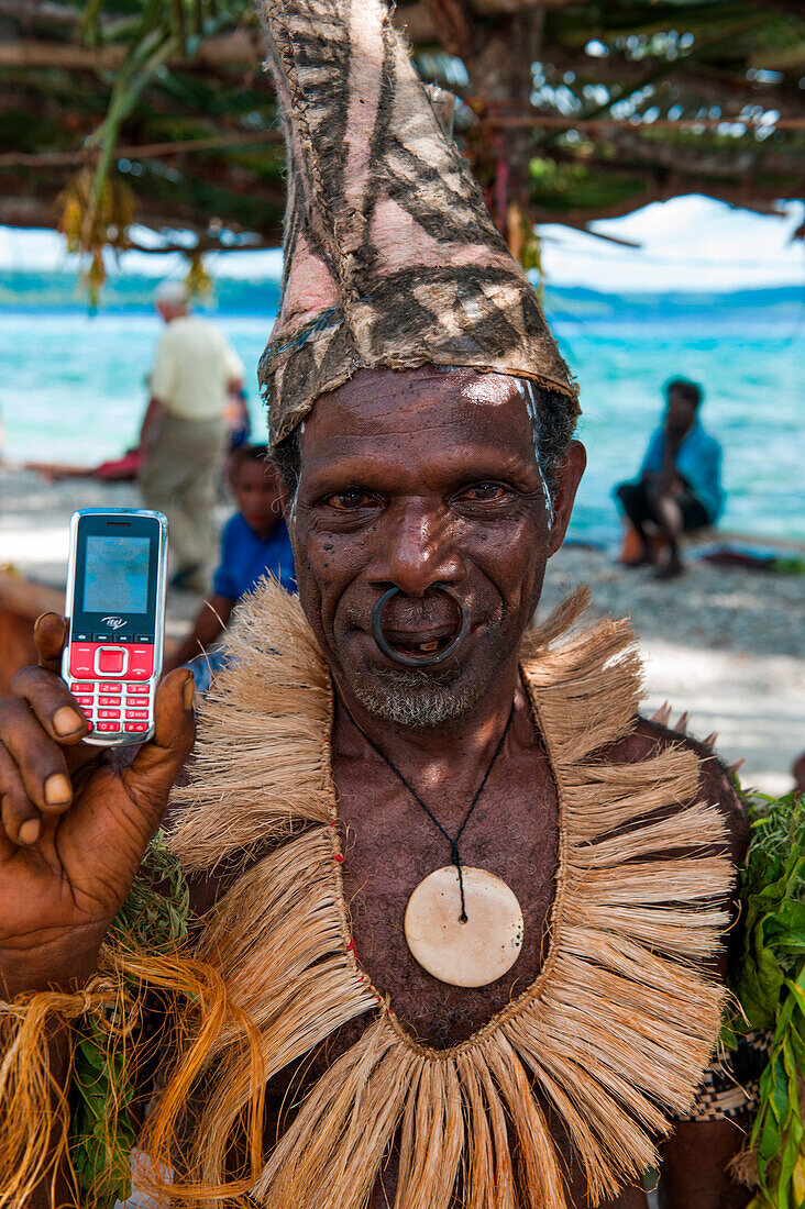 Stammesmitglied in traditionellem Kostüm hält Mobiltelefon, Pigeon Island, East New Britain Provinz, Papua-Neuguinea, Südpazifik