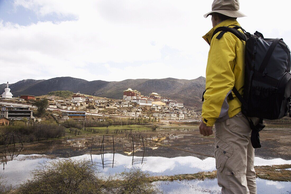 Chinese man trekking and looking at Ganden Sumsteling Gompa (Gandan Sumtseling) (Songzanlin Si) Buddhist Monastery, Shangri-La, formerly Zhongdian, Yunnan Province, China, Asia