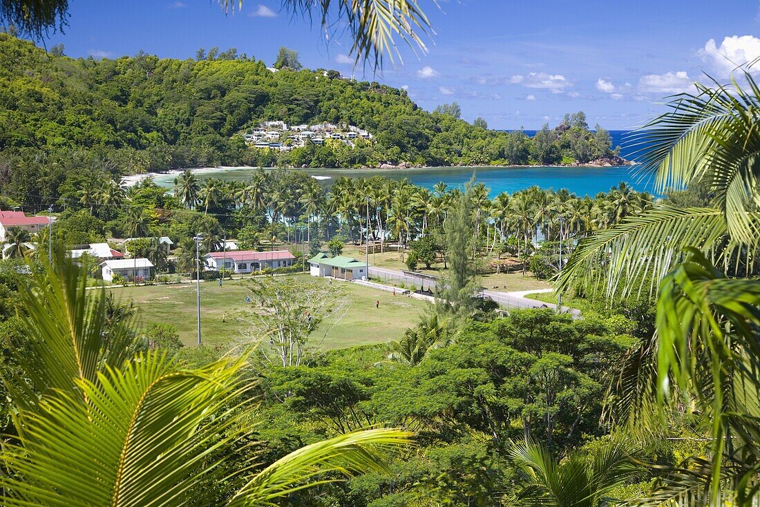 View from hillside across playing field to village and bay, Baie Lazare, Baie Lazare district, Island of Mahe, Seychelles, Indian Ocean, Africa
