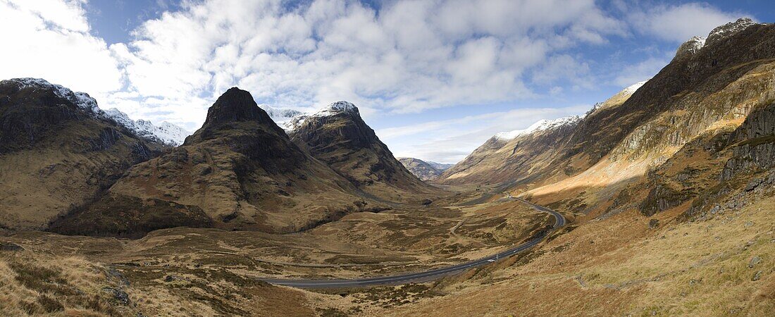 Panoramic view of Glencoe showing The Three Sisters of Glencoe mountains and the A82 trunk road winding down through the glen towards Glencoe Village, near Fort William, Highland, Scotland, United Kingdom, Europe