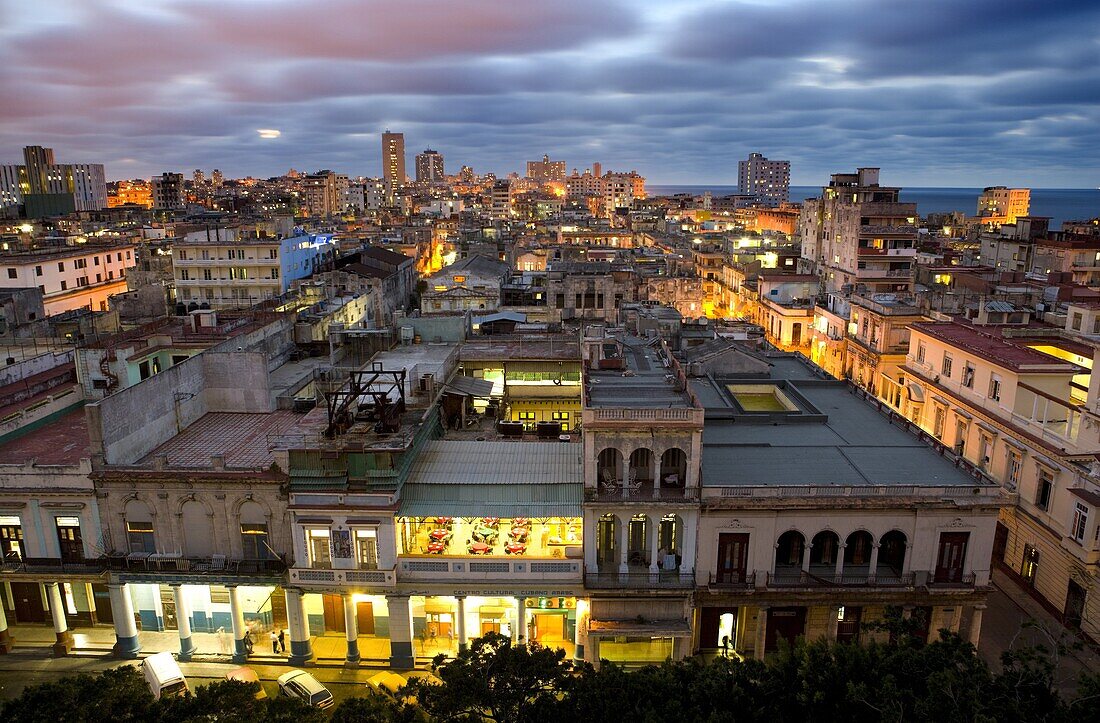 View over Havana Centro at night from 7th floor of Hotel Seville showing contrast of old, semi-derelict apartment buildings against a backdrop of more modern, affluent architecture, Havana, Cuba, West Indies, Central America