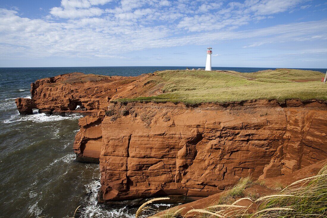 Red sandstone cliff and lighthouse on Cap-aux-Meules Island on the Iles de la Madeleine (Magdalen Islands), Quebec, Canada, North America