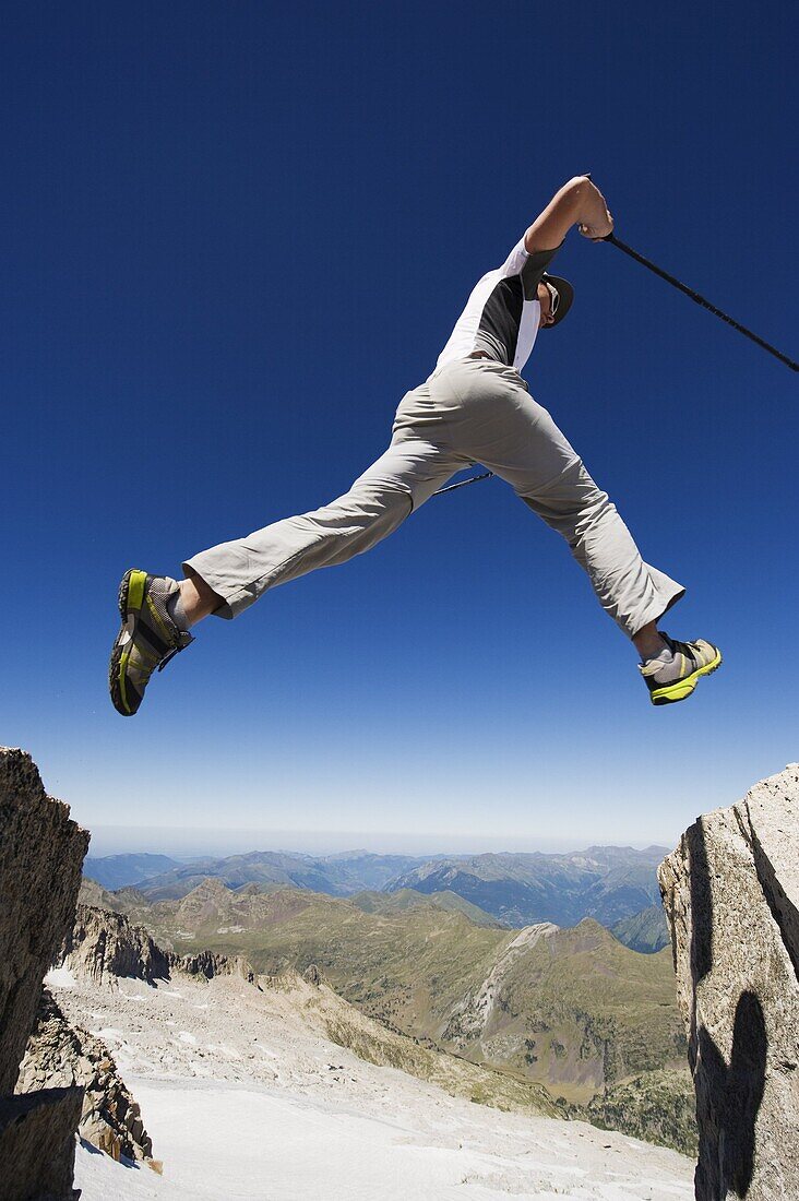 Hiker jumping across a gap in the rocks, Pico de Aneto, the highest peak in the Pyrenees, Spain, Europe