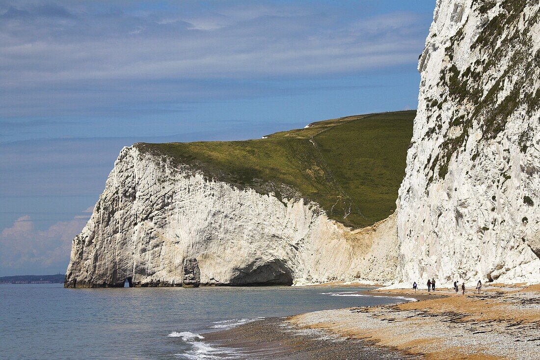 Holidaymakers wander along the beach at Durdle Door, towards Bats Head Cliff, Dorset, England, United Kingdom, Europe