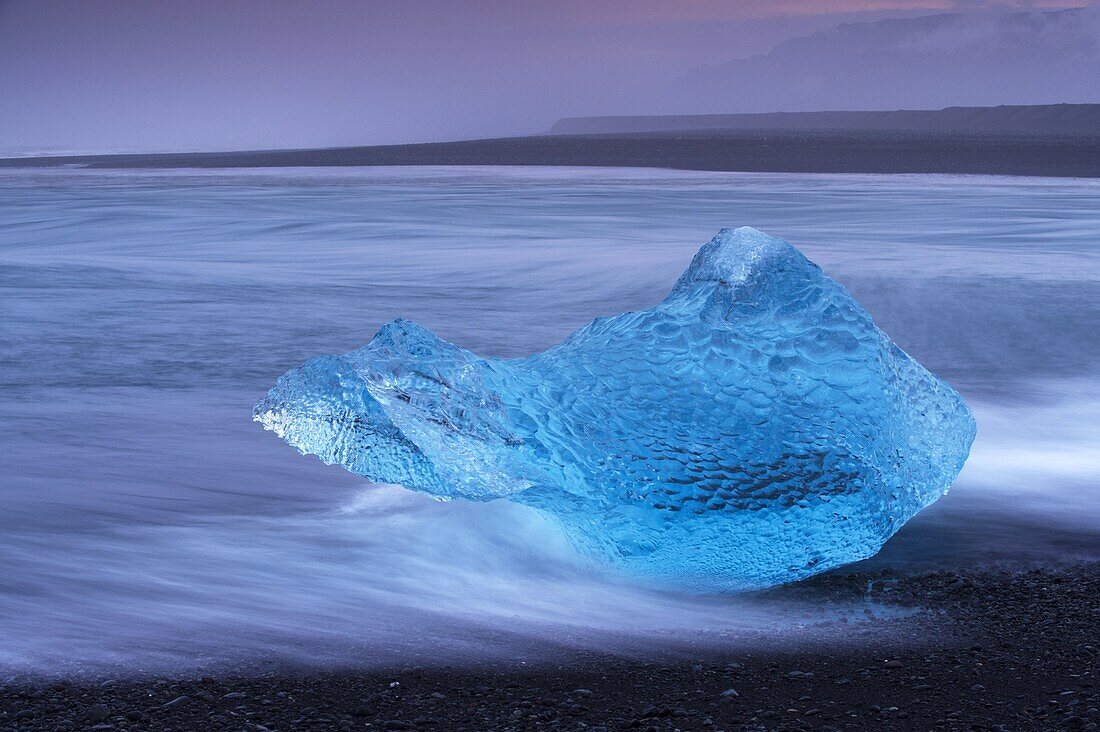 Translucent blue iceberg washed ashore on Breidamerkursandur black sands, near Jokulsarlon glacial lagoon, East Iceland, Polar Regions