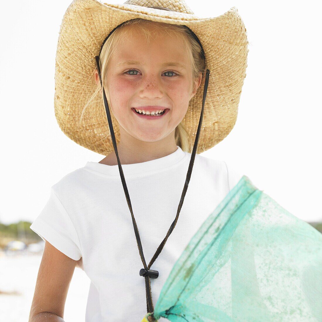 Girl (6-8) on beach wearing straw hat, carrying fishing pole