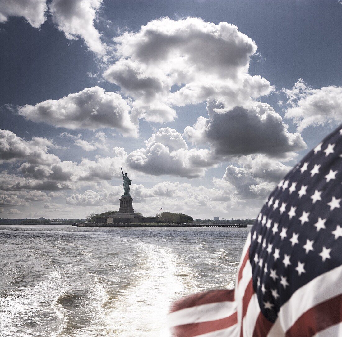 View of Statue of Liberty from rear of bot with Stars and Stripes flag, New York, United States of America, North America