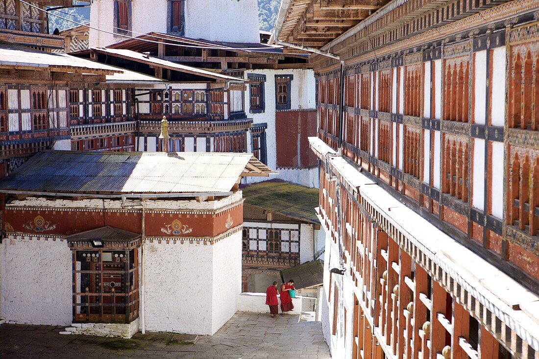Two Buddhist monks chatting against the imposing backdrop of Trongsa Dzong, Trongsa, Bhutan, Asia