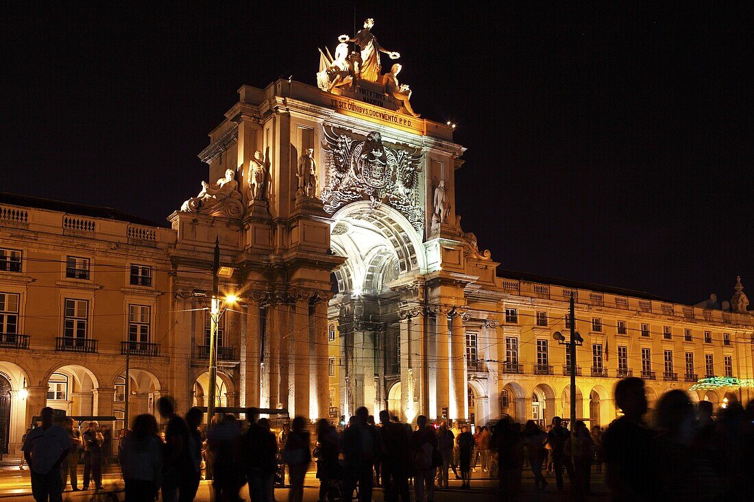 Silhouetted people on Praca do Comercio square under the illuminated Rua Augusta Arch at night in central Lisbon, Portugal