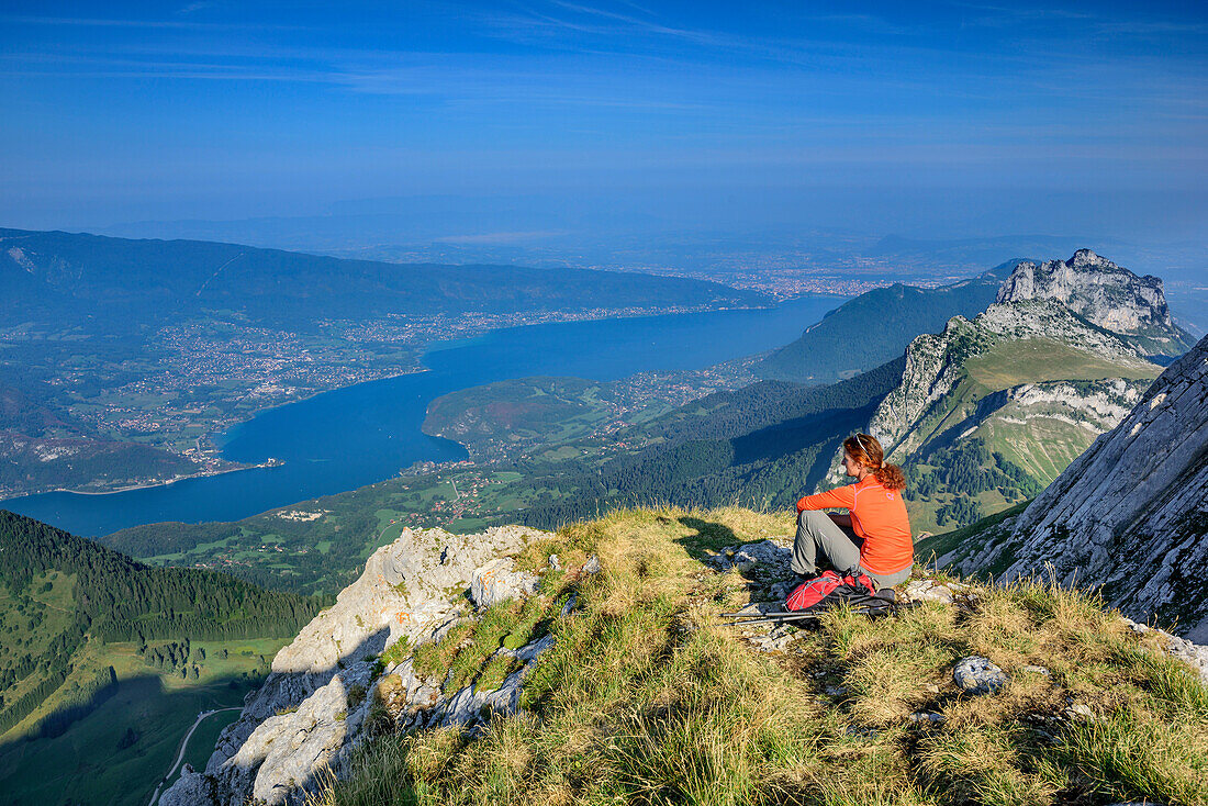 Frau beim Wandern sitzt auf Grasabsatz und blickt auf Lac d'Annecy, La Tournette, Hochsavoyen, Frankreich