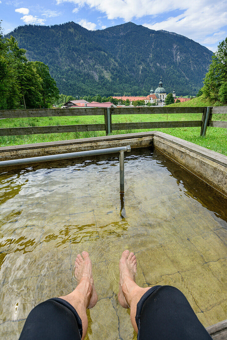 Person kühlt Beine im Kneippbecken, Ettal im Hintergrund, Ettal, Ammergauer Alpen, Oberbayern, Bayern, Deutschland