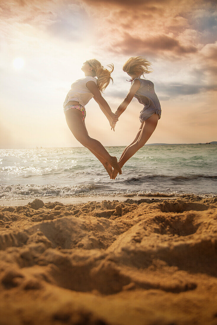 Zwei junge Frauen springen vom Strand in die Luft und formen dabei ein Herz, 'S Arenal, Palma, Mallorca, Balearic Islands, Spain