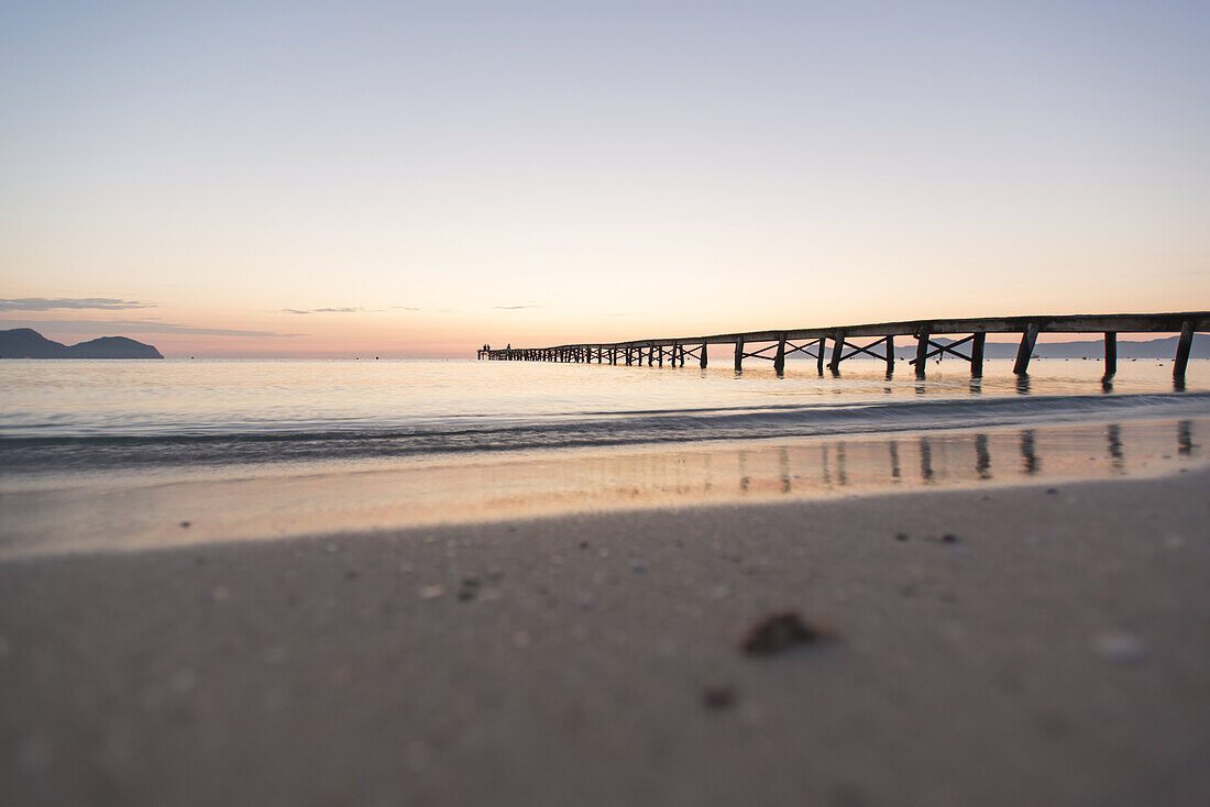 Pärchen sitzt am Ende eines langen Steg in der Morgenstimmung. Strand Playa de Muro, Alcudia, Mallorca, Balearen, Spanien