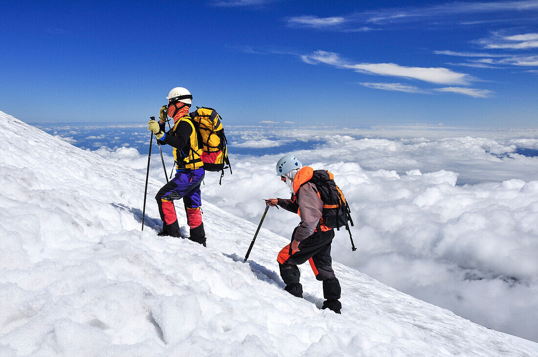 Mountain climbers with ice axe on snow field over the clouds, volcano Villarrica, Strato volcano, sunset, National Park Villarrica, Pucon, Región de la Auracania, Region Los Rios,  Patagonia, Andes, Chile, South America