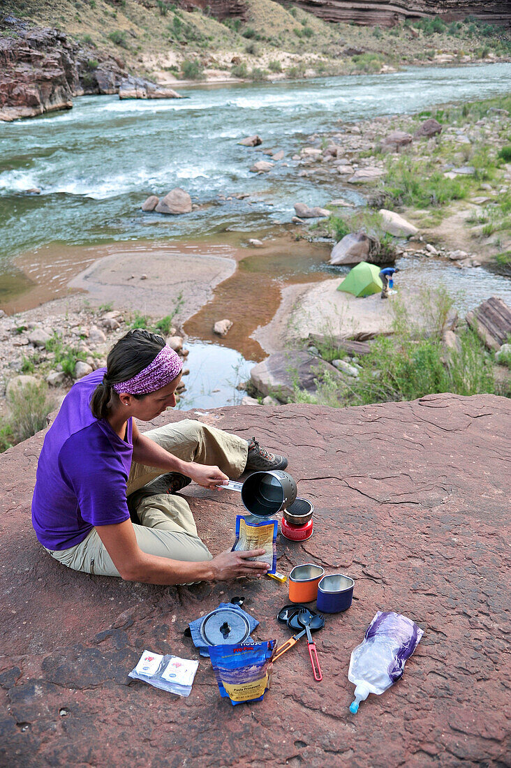 Female hiker cooks dinner on a cliff-pinched patio above camp and the Colorado River near Deer Creek Falls in the Grand Canyon outside of Fredonia, Arizona November 2011.  The 21.4-mile loop starts at the Bill Hall trailhead on the North Rim and descends 