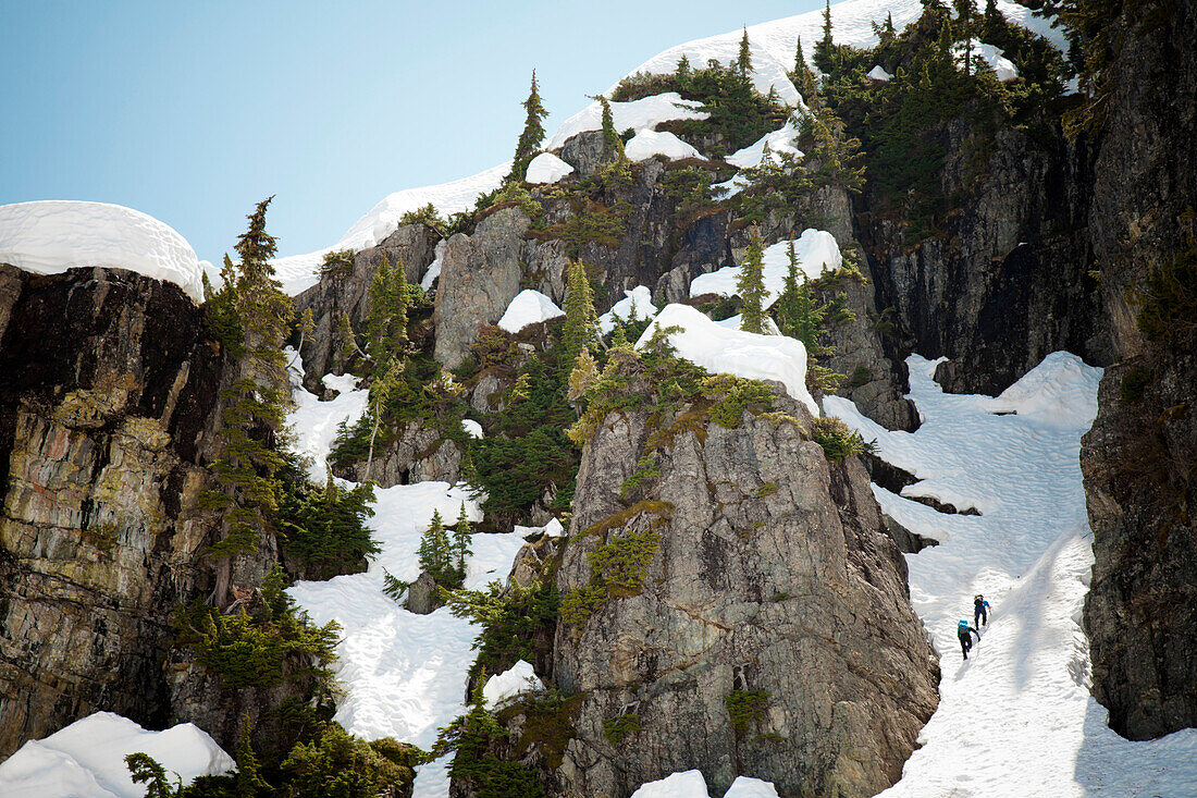 Two backpackers climb a snow filled gully high in the mountains of British Columbia, Canada.