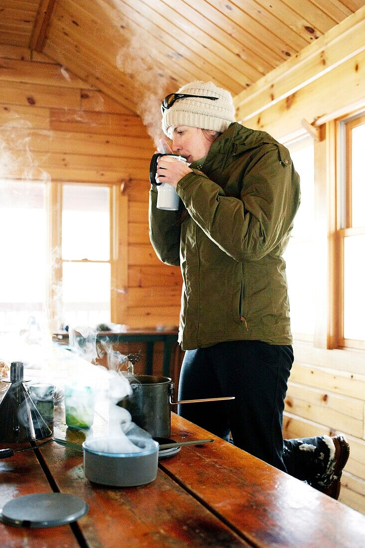 A young woman drinks a hot drink while waiting for her cabin to warm up. Baxter State Park, Maine.