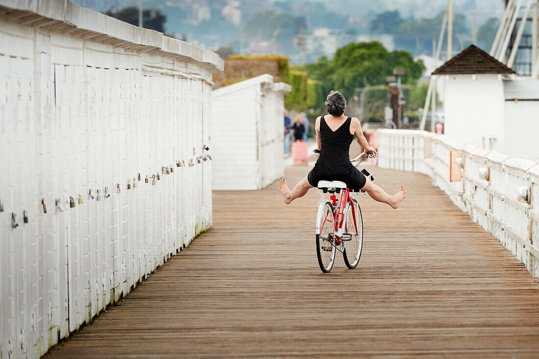 Older Caucasian woman riding bicycle on wooden dock